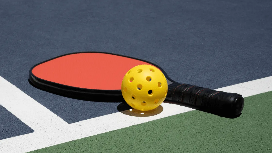 Orange pickleball paddle on a blue court next to a yellow ball